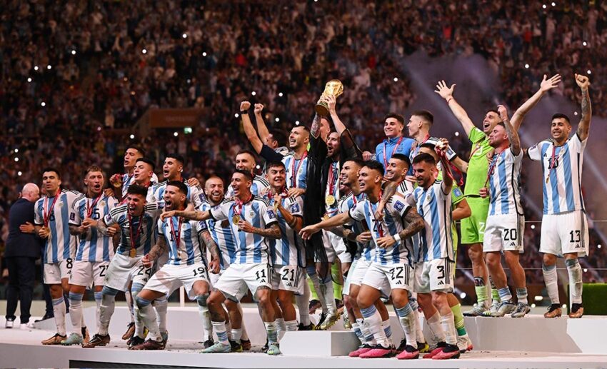 The Argentina national football team celebrating with the World Cup trophy on the podium after their 2022 victory.