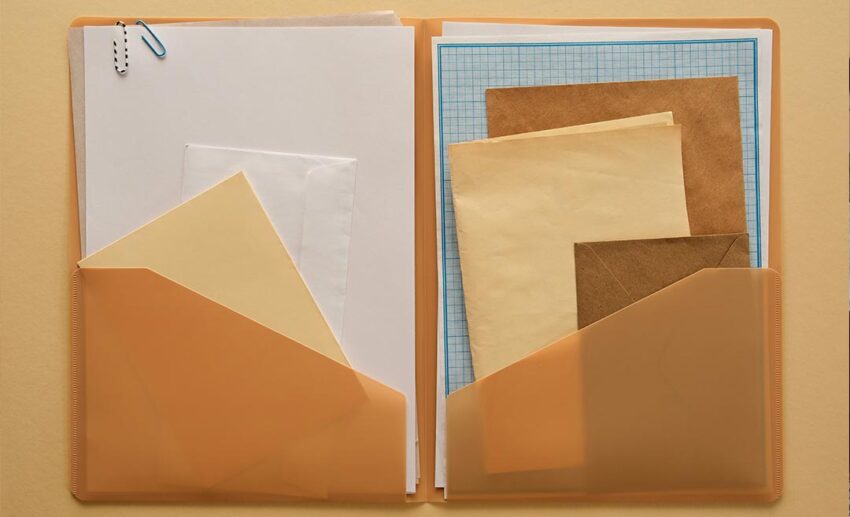 An open physical folder containing travel documents, printed itineraries, and a metal clip on a desk.