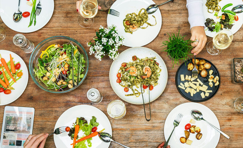 An overhead view of a diverse dinner table laden with pasta, salad, and a variety of dishes as friends celebrate.