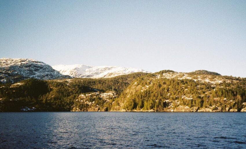 A scenic winter landscape of the Norwegian fjords featuring dramatic mountains and the serene, cold waters of the North Sea.