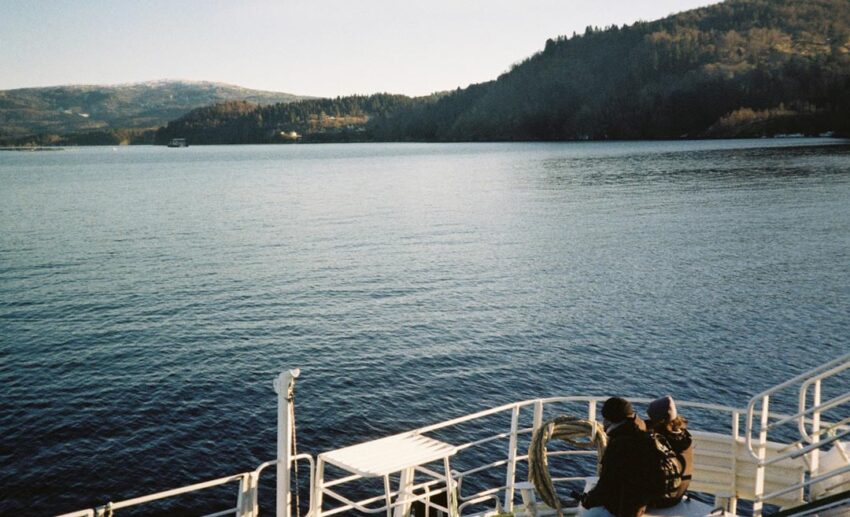 A view from a boat deck looking out onto the deep blue waters and rugged coastline of a Norwegian fjord during a winter tour.