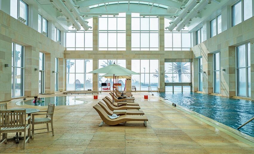A spacious indoor swimming pool with lounge chairs and umbrellas, offering a shaded cooling option.