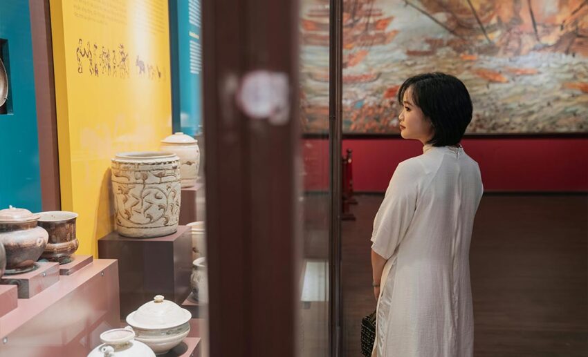 A woman standing in a quiet museum gallery, thoughtfully contemplating ancient artefacts in a glass display case.