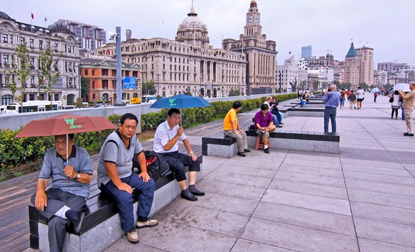 Tourists and locals seated at a pedestrian section of the Bund in Shanghai, China, with some people holding umbrellas.