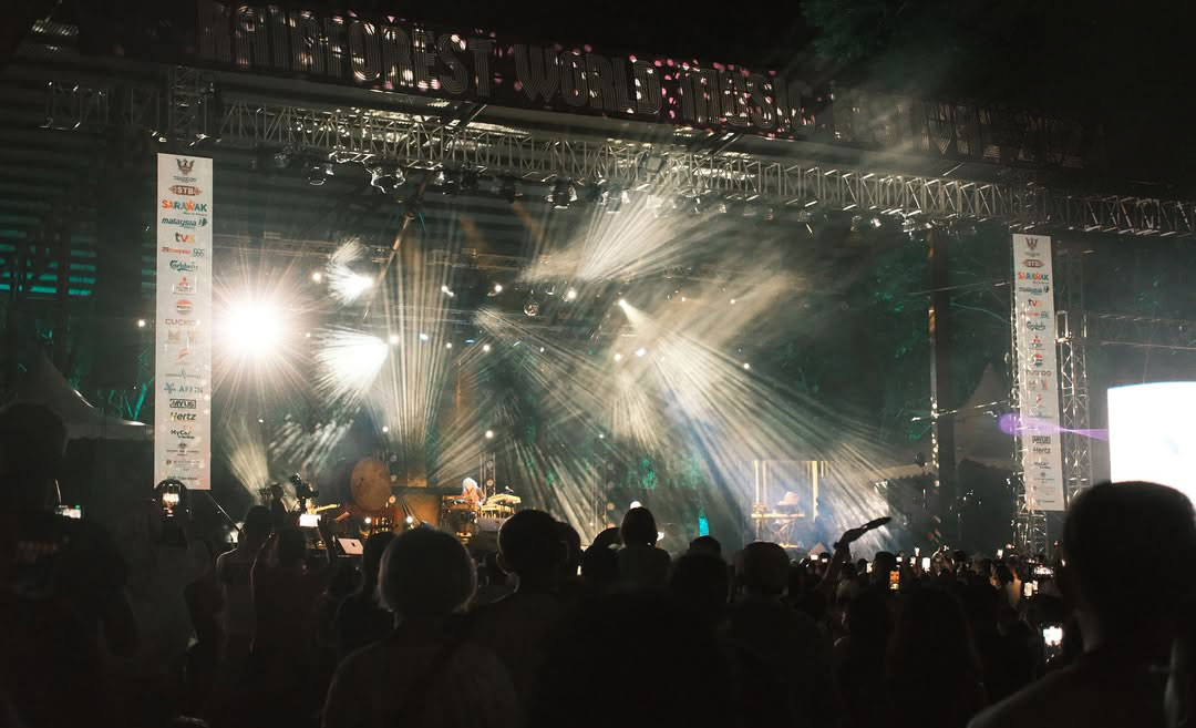 A wide night-time shot of a lively musical performance on the main stage of the Rainforest World Music Festival (RWMF) in Sarawak, Malaysia.
