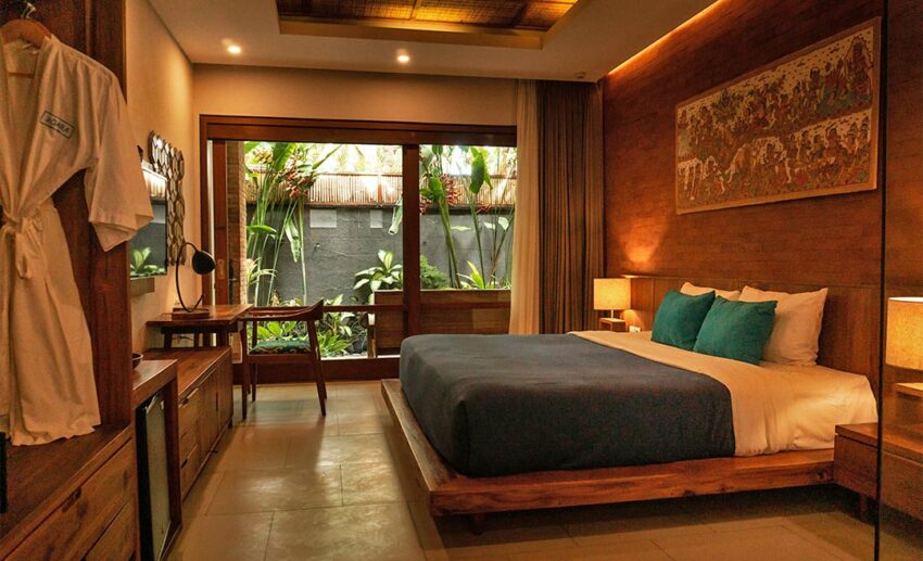 A modern boutique hotel room with a wooden bed frame, large glass doors, and visible greenery to promote natural ventilation.