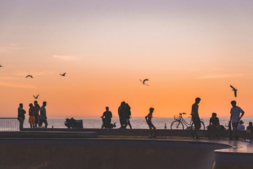 Silhouettes of people walking and skateboarding against a vibrant orange sunset at Scarborough Beach in Western Australia.