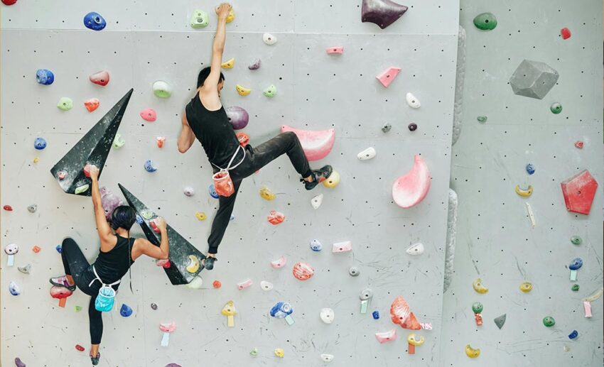 Two people indoor rock climbing on an artificial wall with colourful handholds, practicing with a coach.