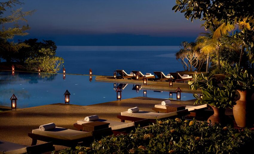 The swimming pool at Tanjong Jara Resort at dusk, featuring still water and glowing traditional lanterns under a twilight sky.
