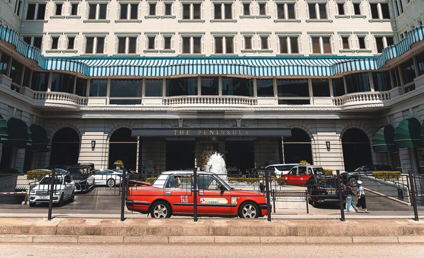 The Peninsula Hotel Hong Kong entrance with red taxis and cars, showcasing hotel-provided transportation services.