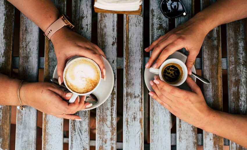 A vertical close-up of two female friends having a coffee and cappuccino break together at a cafe bar.