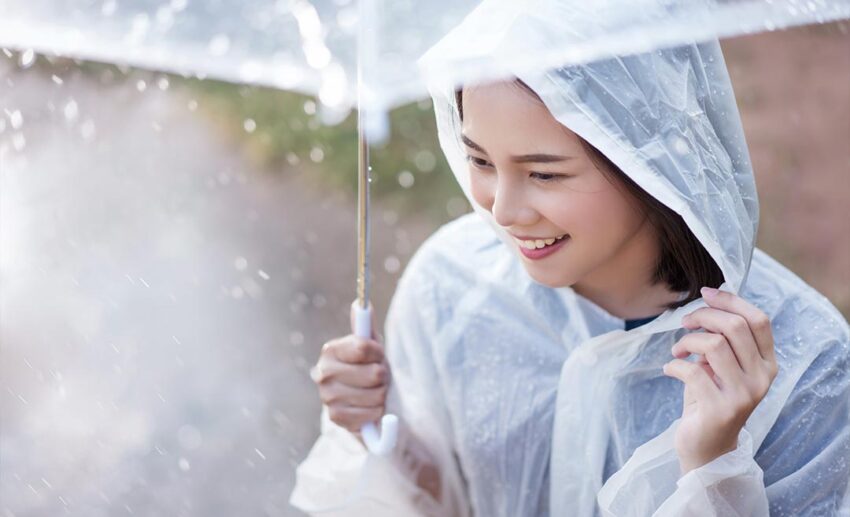 A smiling Asian woman wearing a raincoat outdoors during a rainy day at a festival in the Sarawak rainforest.