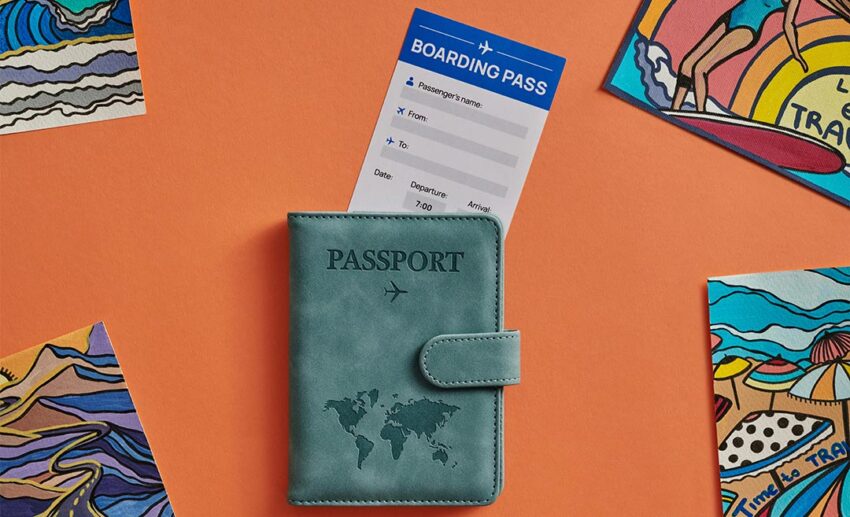 A flat lay photo on an orange background featuring a light green passport holder with a boarding pass and travel-themed paintings.