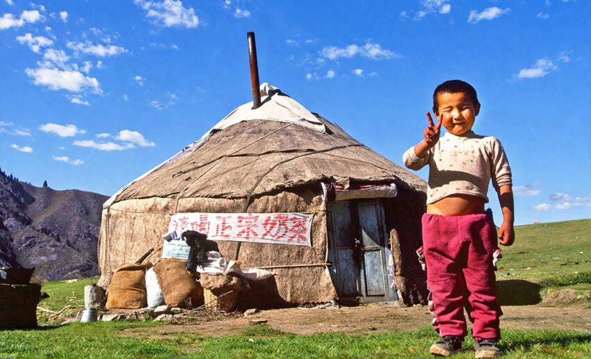 A young boy posing happily in front of a traditional yurt in Urumqi, China.