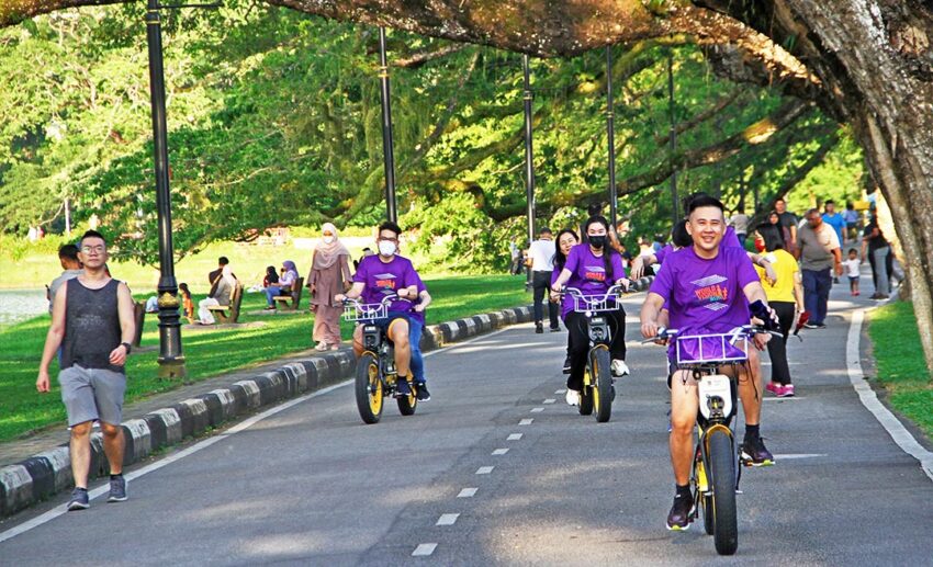 People walking and cycling along the paved paths of Taiping Lake Gardens under the shade of ancient rain trees.