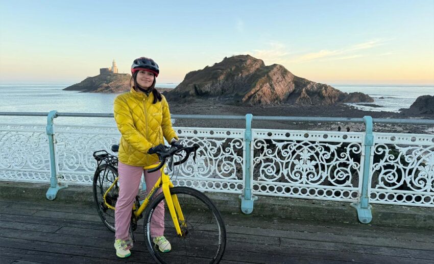 Sofia cycling along the coastal path in Mumbles with the sea and sky in the background.
