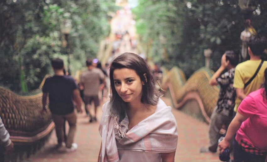 A solo female traveller smiling at the camera at the top of the open-air staircase at Wat Phrathat Doi Suthep temple in Chiang Mai, Thailand.