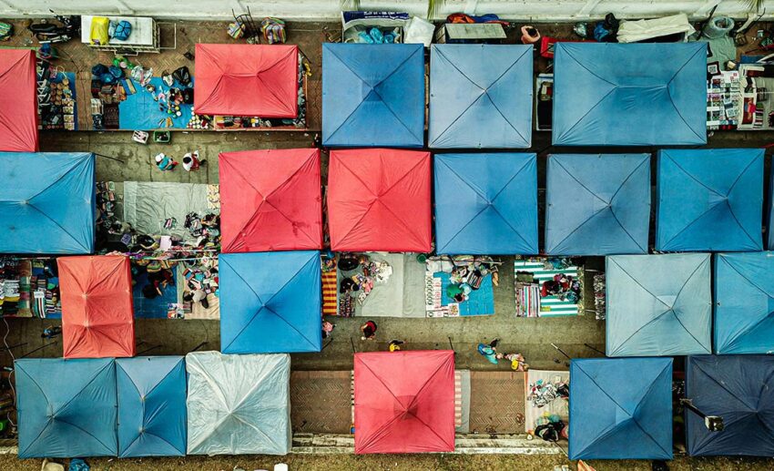 A high-angle view of the Luang Prabang night market, showing the iconic red, blue, and white umbrella tops of the vendor stalls.