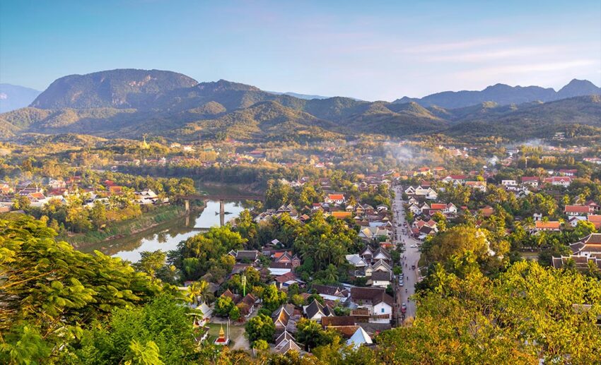 A panoramic sunset view over the historic town of Luang Prabang, Laos, and the surrounding Mekong River valley.