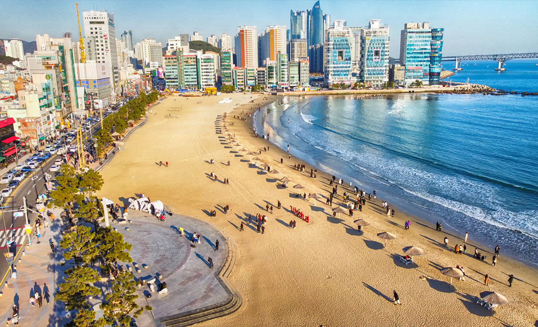 Aerial view of Gwangalli Beach in Busan, South Korea, during winter, showing the calm blue ocean and sandy shoreline from above.