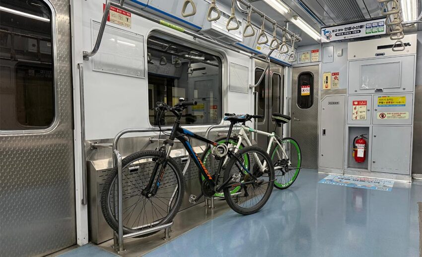 Bicycles parked, secured with belts in a designated bike rack area inside a South Korean train carriage.