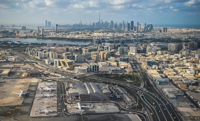 Stunning high-angle aerial view of the Dubai cityscape and airport in the foreground, with iconic skyscrapers stretching into the distance.