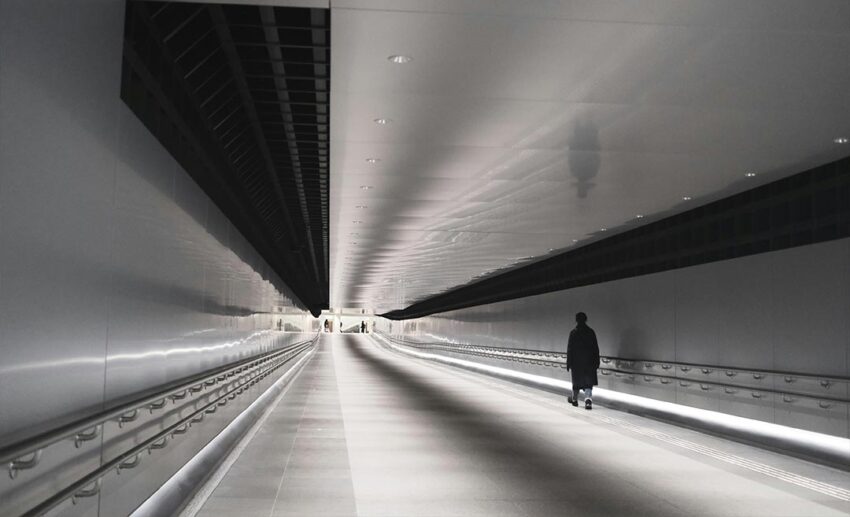 A lone man walking down a long, modern pedestrian tunnel in the Ginza Six district of Tokyo.