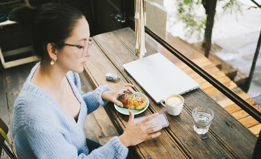 A woman enjoying a quiet breakfast at a cafe while looking at her phone at the start of her day.