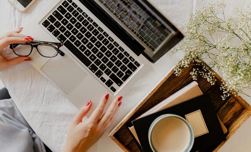Close-up of a woman’s hand using a laptop at a desk with a cup of coffee, representing flight research and booking.
