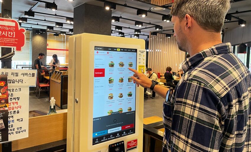 A person using a digital self-order kiosk at a Korean restaurant with an English language option visible on the screen.