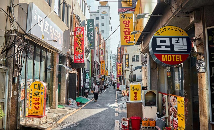 A narrow urban street in Korea filled with colourful shop signs and a prominent sign for a motel.