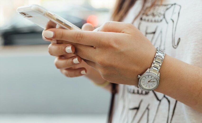 A woman holding an iPhone outdoors during the day, using it to manage her digital travel documents and arrival cards.