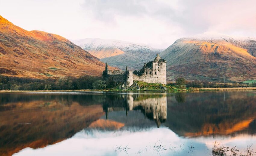 The historic stone ruins of Kilchurn Castle near a lake in the Scottish Highlands under a soft grey autumn sky.