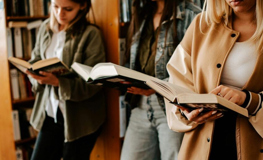 Two women standing close together while holding open books, sharing a moment during a buddy-read session.