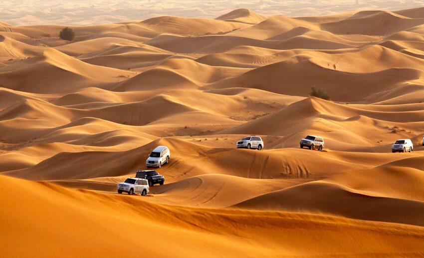 Several 4WD off-road vehicles driving through a vast, arid desert landscape under extreme summer conditions.