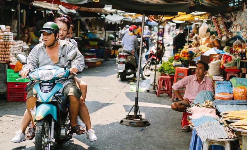 Local commuters on motorbikes passing through the busy Tân Định Market in Ho Chi Minh City at dawn.