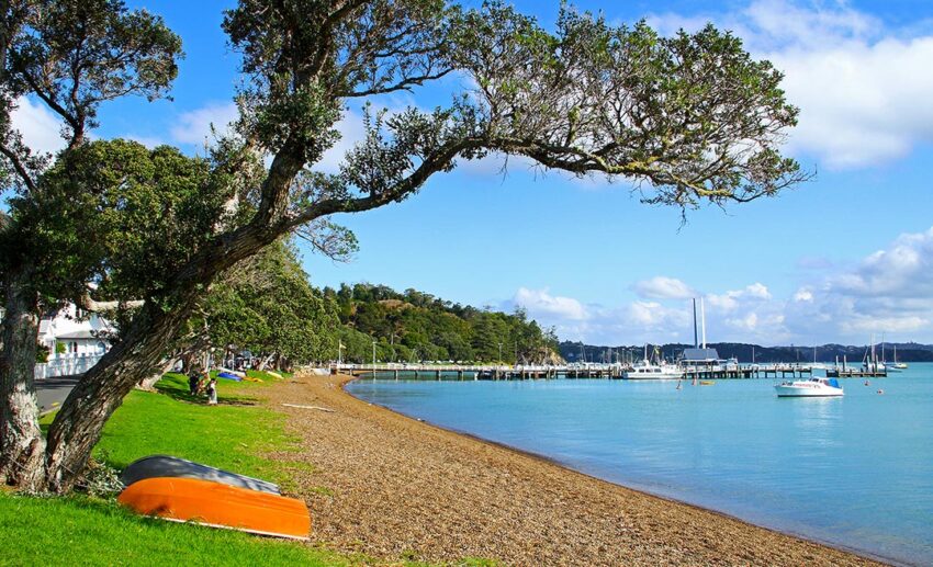 A peaceful daytime view of the bayside beach in Russell, Bay of Islands, New Zealand, with small boats floating on still, calm water.