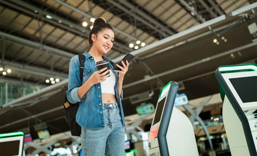 A smiling young Asian female traveller holding her smartphone and checking her online registration and map location for a trip abroad.