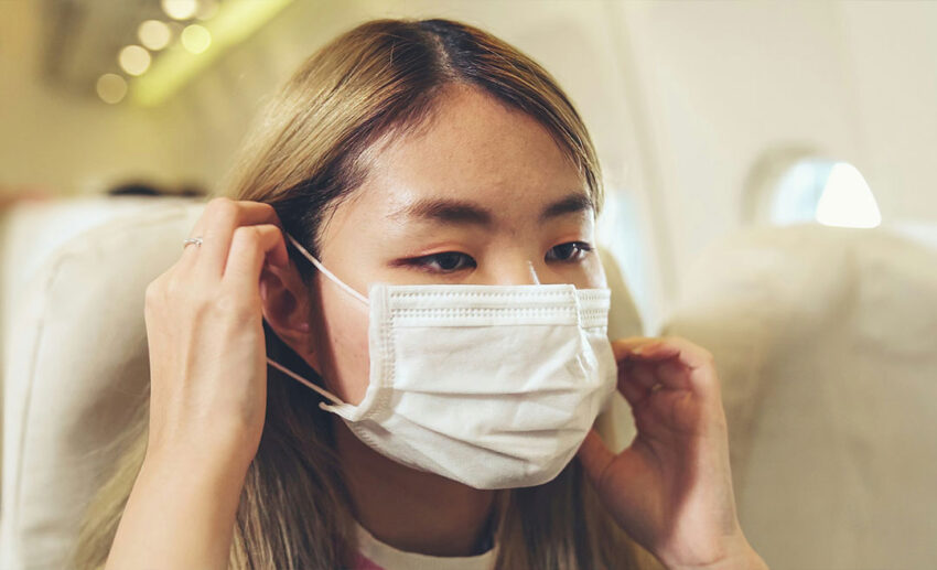 A traveller wearing a protective face mask while sitting in a seat on a commercial airplane during a flight.