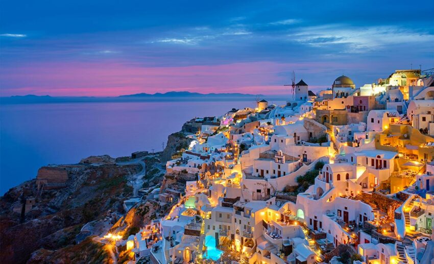 The traditional white houses and windmills of Oia village in Santorini, Greece, captured during the cool evening golden hour.