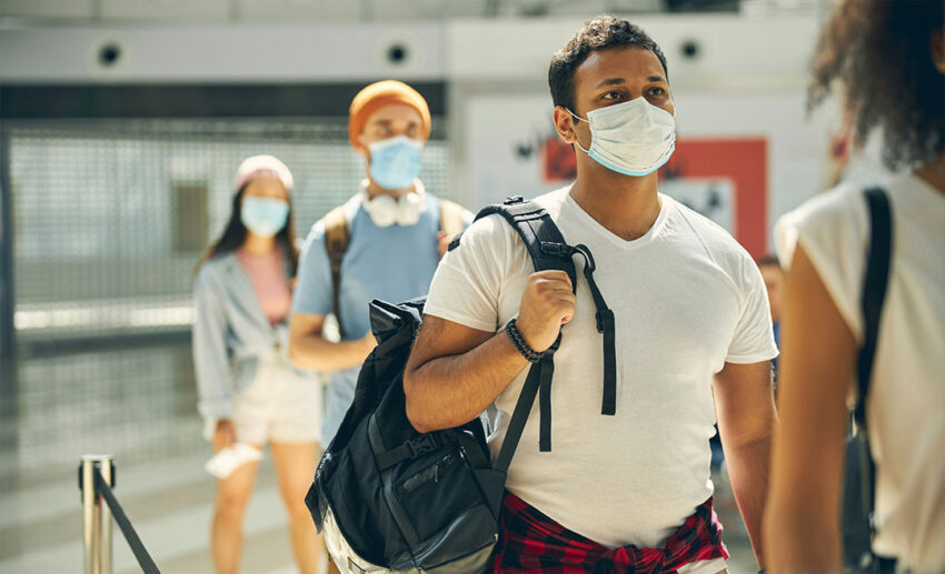 A man in a white shirt with a backpack on his shoulder standing in an airport terminal, waiting to board a flight for international travel.