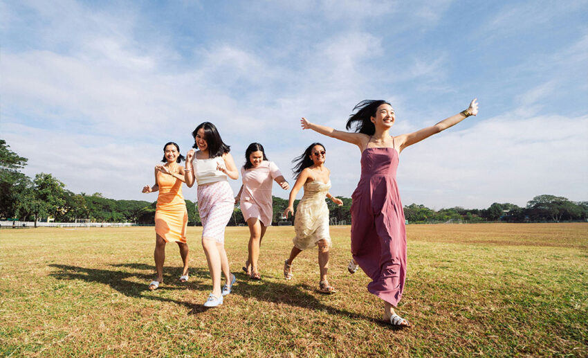 A group of diverse women running joyfully across a lush green grass field during a group trip.