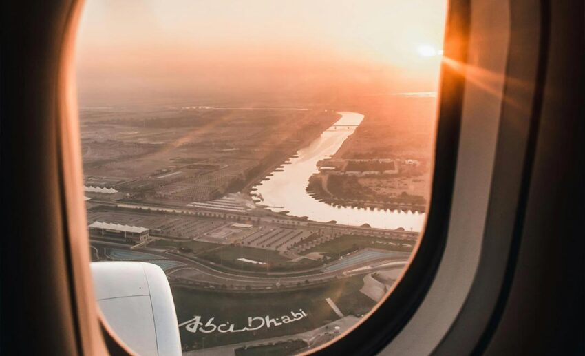 Captivating aerial sunset view over Abu Dhabi as seen through an airplane window, symbolising the cautious optimism of returning flight paths.