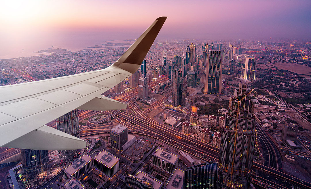 Aerial view of the Dubai skyline at twilight from an airplane window, with the wing visible against a purple sky.