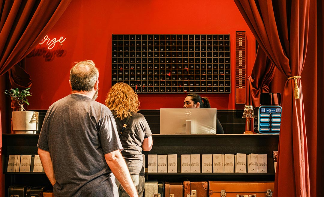 A couple in travel attire checking in at a beautifully designed, vintage-style hotel reception desk, illustrating the modern hotel check-in experience.