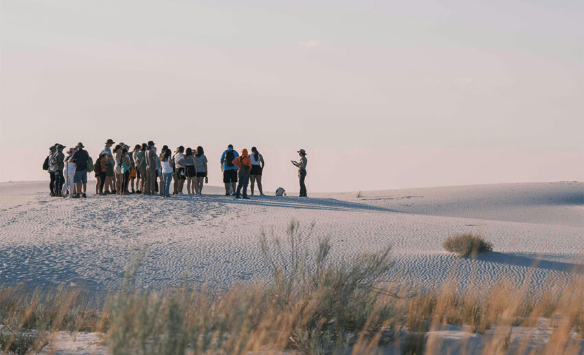 A group of tourists gathering on the white dunes of White Sands National Park, New Mexico, during a guided desert excursion.