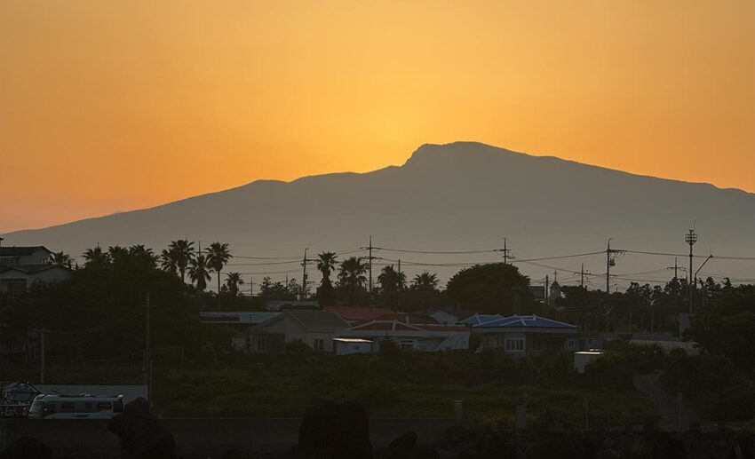The dark, dramatic silhouette of Mount Hallasan, South Korea's highest volcanic mountain peak, standing tall against a fading sky.