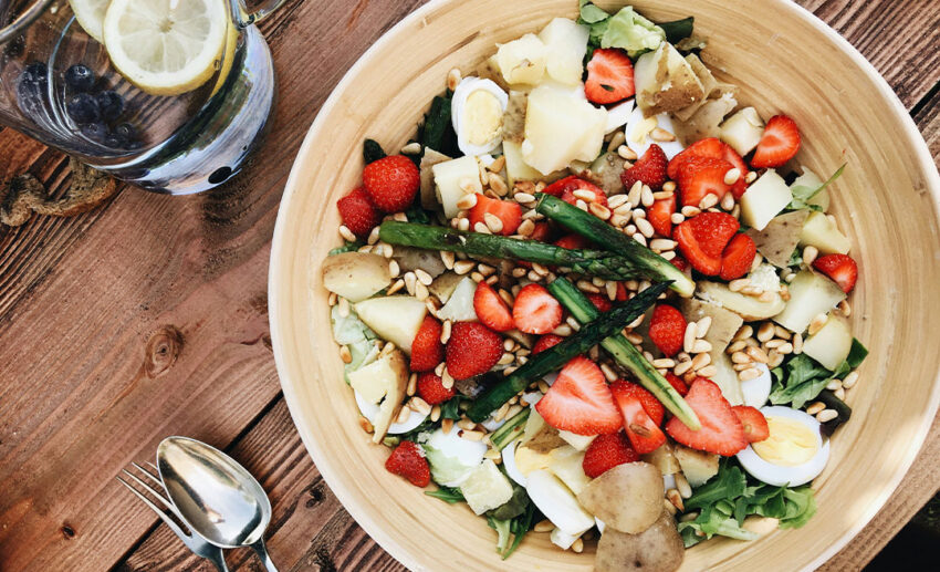A fresh sliced strawberry salad dish in a white ceramic bowl next to a spoon, representing locally sourced food during a slow travel trip.