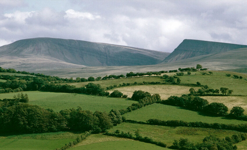 Lush green fields leading to the rugged Black Mountain vista and sweeping valley terrain in the Brecon Beacons National Park, Wales.