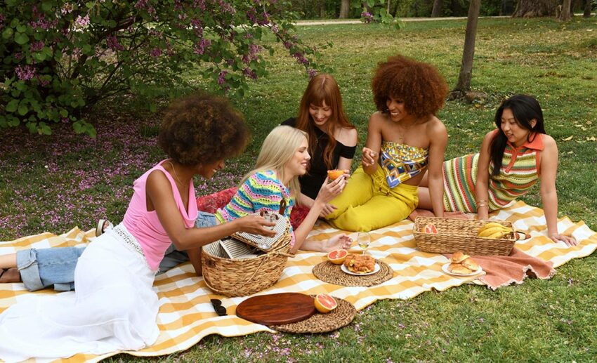 A supportive community of women laughing and sharing food during an outdoor park picnic, illustrating expat networking and friendships abroad.